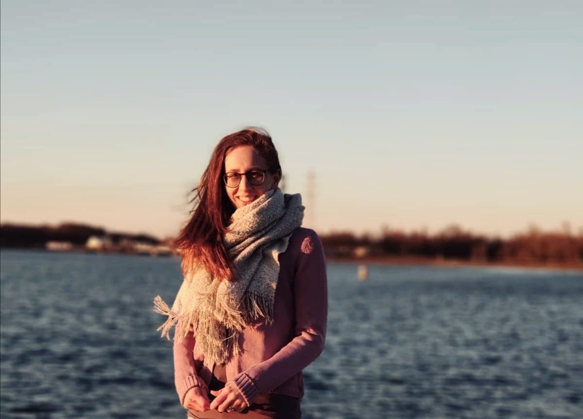 Bianca Braun, lächelnd mit Schal vor einem See im Abendlicht