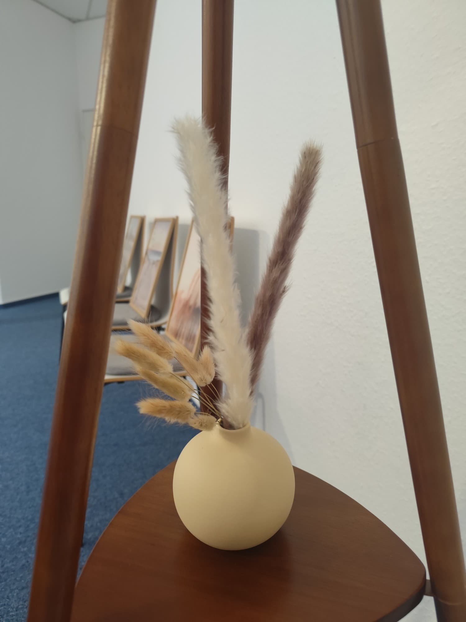 Beigefarbene Vase mit Trockenblumen auf einem Holztisch im Praxisraum